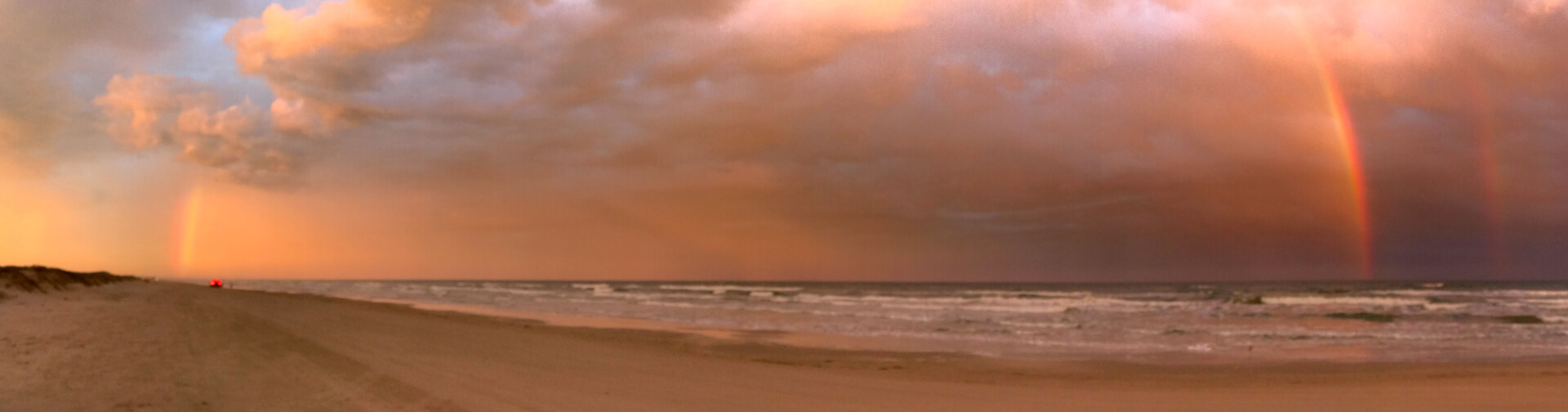 car driving on the beach into a rainbow